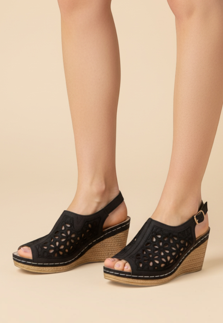 Falio women's black faux leather wedge sandals with laser-cut floral patterns and an 8cm heel on a beige background.