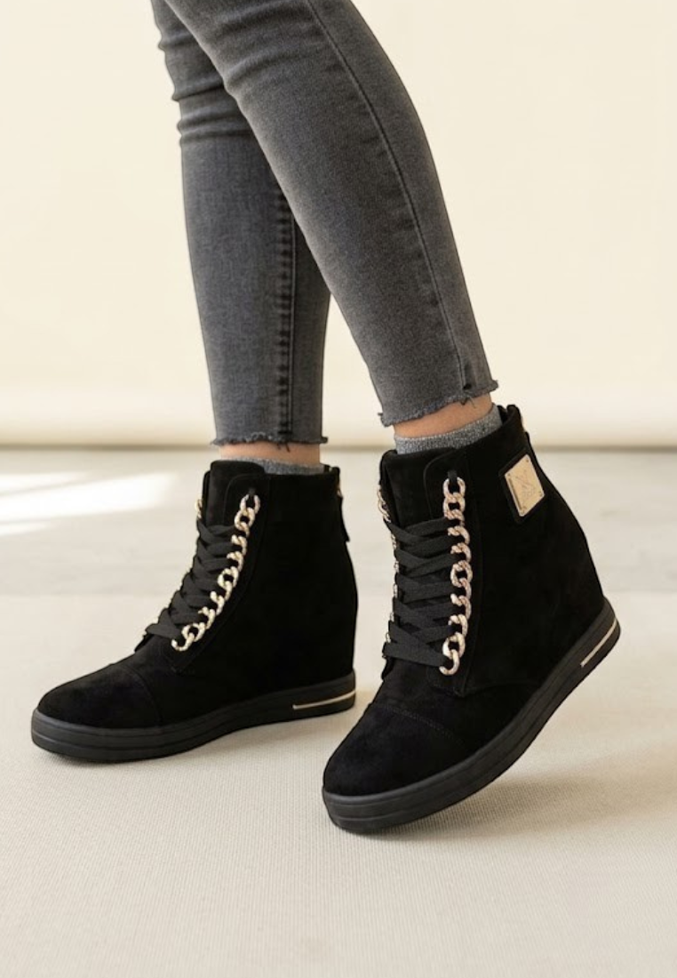 Falio black faux suede wedge sneakers with gold chain detail and lace-up closure worn by a woman