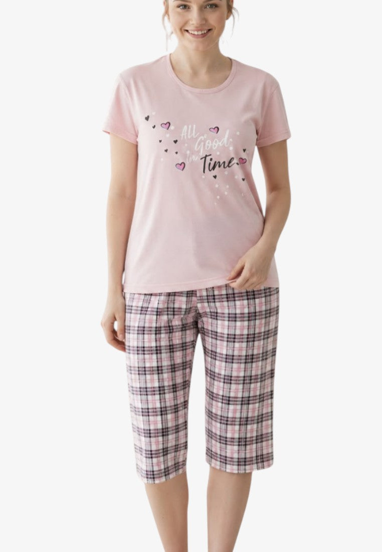 Lifestyle shot of a pink pajama set with short sleeves and checked shorts on a white background.