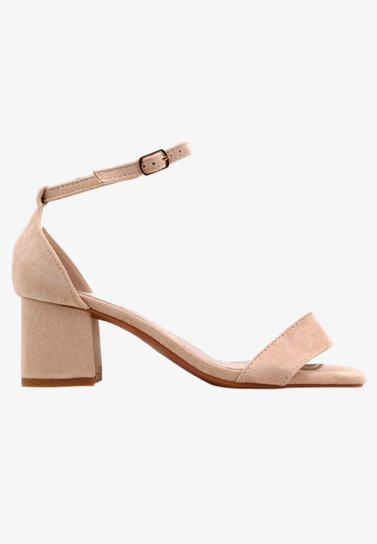 Boczne ujęcie beżowych sandałów damskich na słupku z paskiem wokół kostki na białym tle