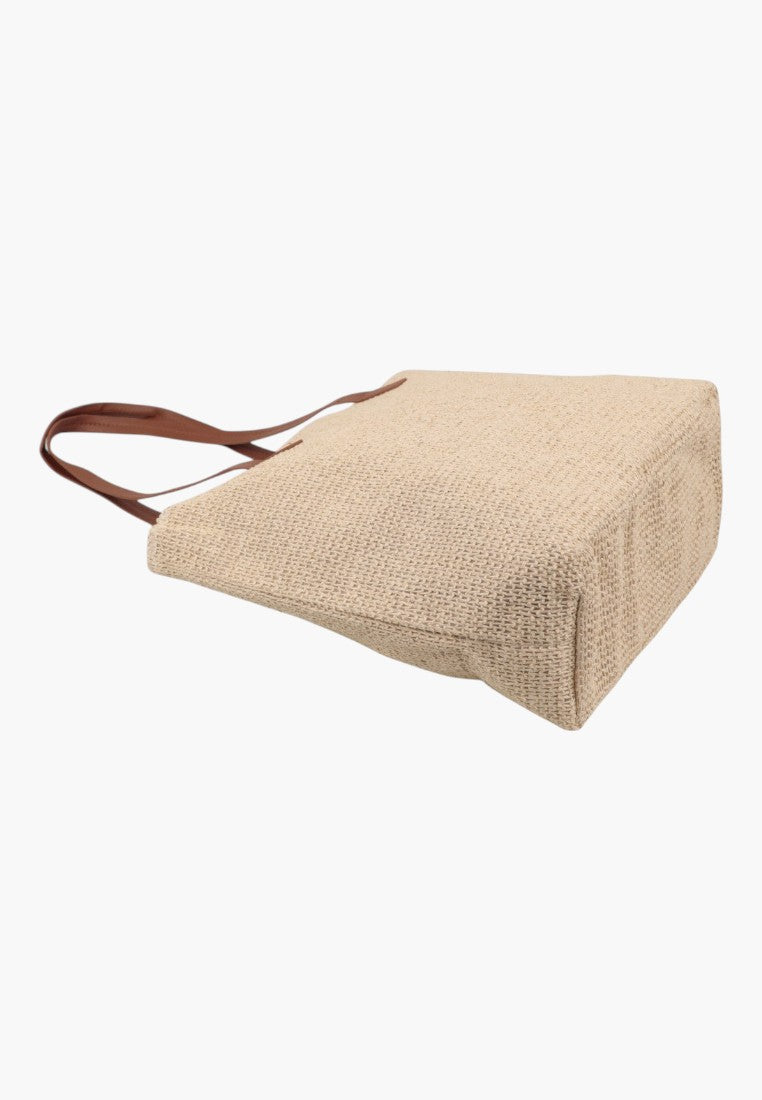 Z boku beżowej torebki damskiej shopper z miękkiego materiału na białym tle