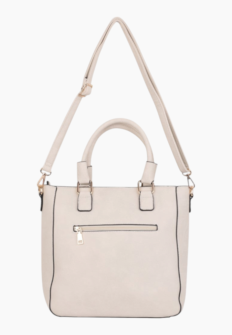 Back view of a cream handbag with adjustable strap and tassel charm.