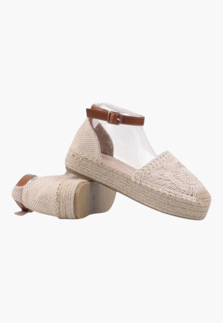 Back view of beige sandals with ankle strap and textured surface.