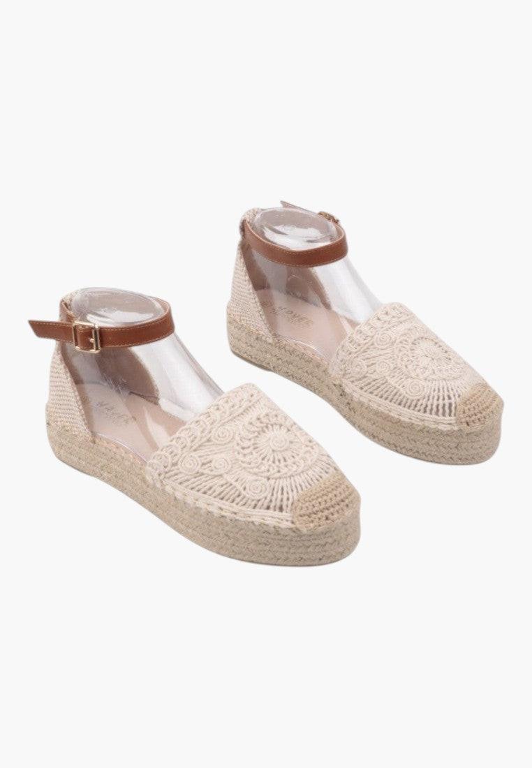 Front view of beige sandals with ankle strap and textured surface.