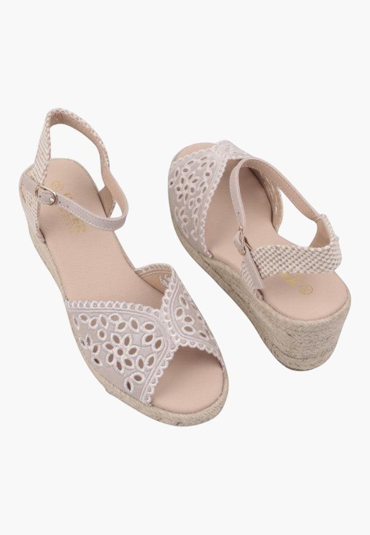Close-up detail of beige wedge sandals with textured upper and platform sole on a white background