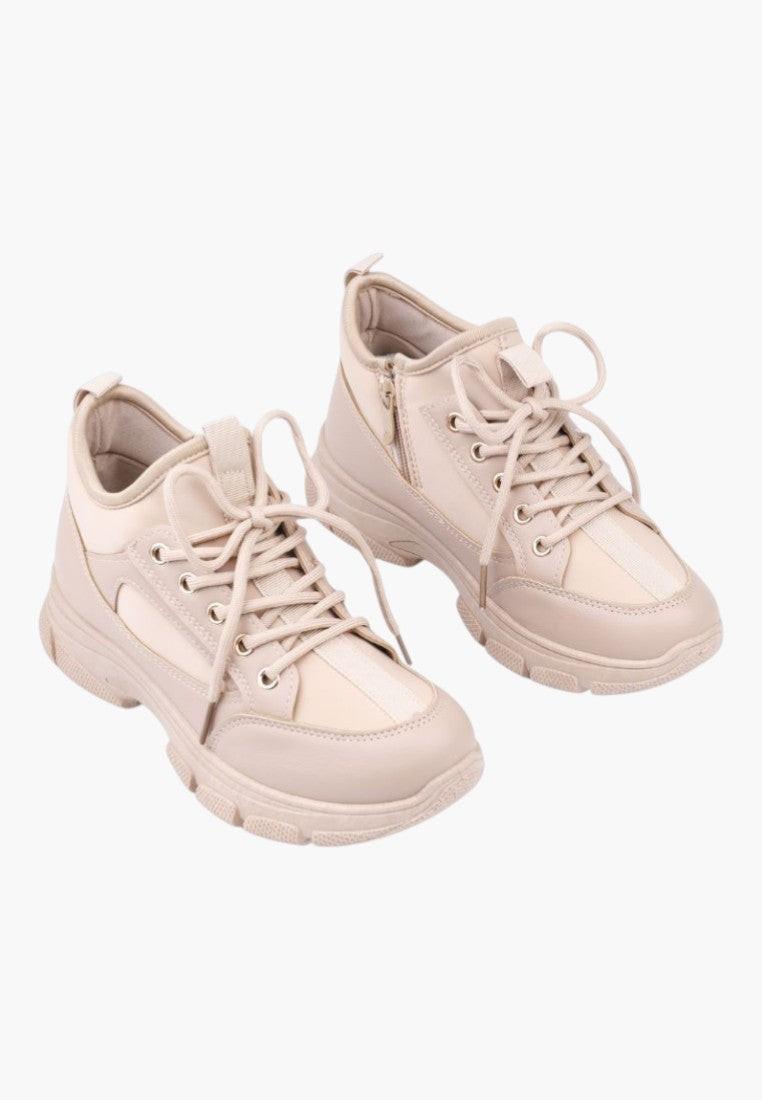 Lifestyle shot of beige sneakers with a lace-up design on a white background.