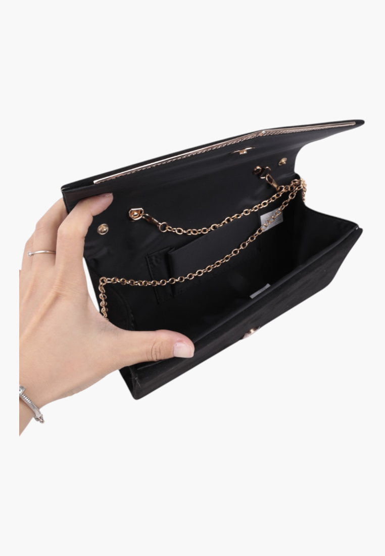 Detail view of the black faux leather clutch held in a hand, showcasing the gold chain strap.