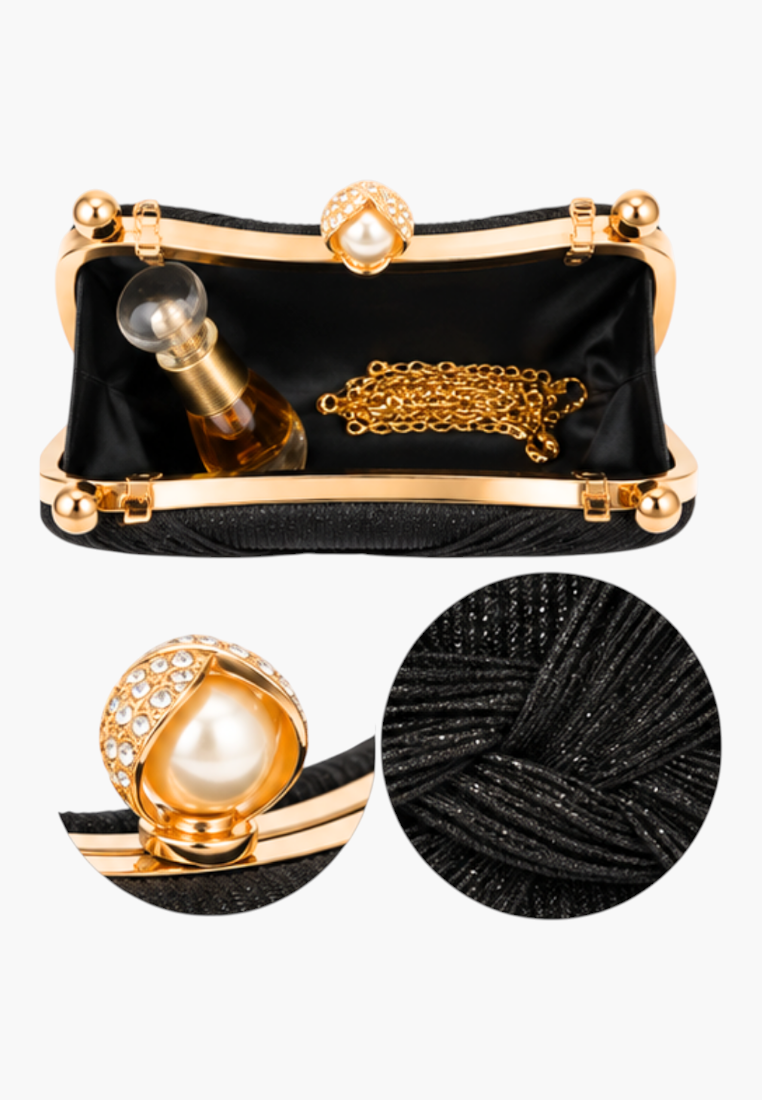 Detail view of the black clutch bag with gold hardware and pearl accent on textured fabric.