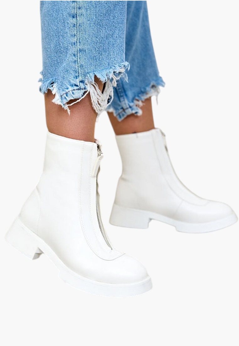 Lifestyle view of white ankle boots with zipper closure and chunky heel on a natural background.
