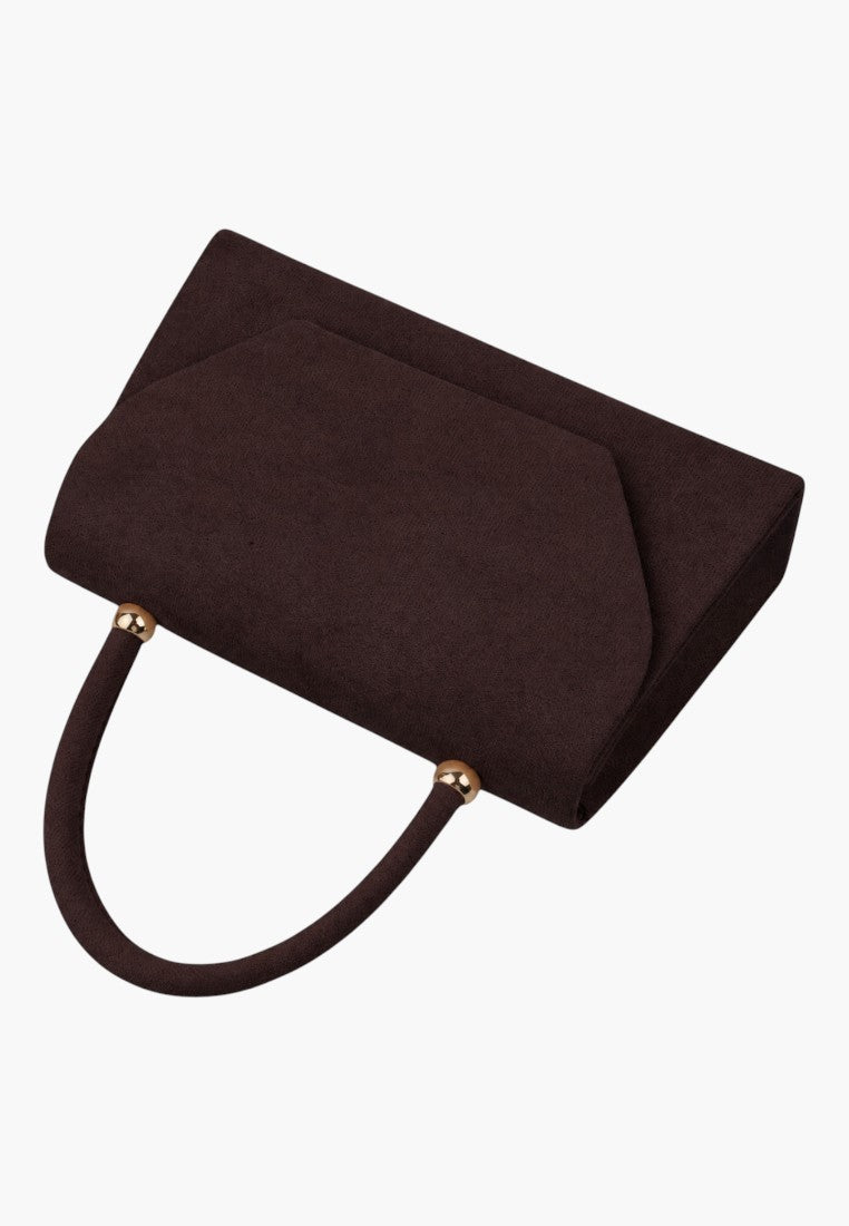 Detail close-up of a brown handbag with a textured surface and flap closure on a white background.