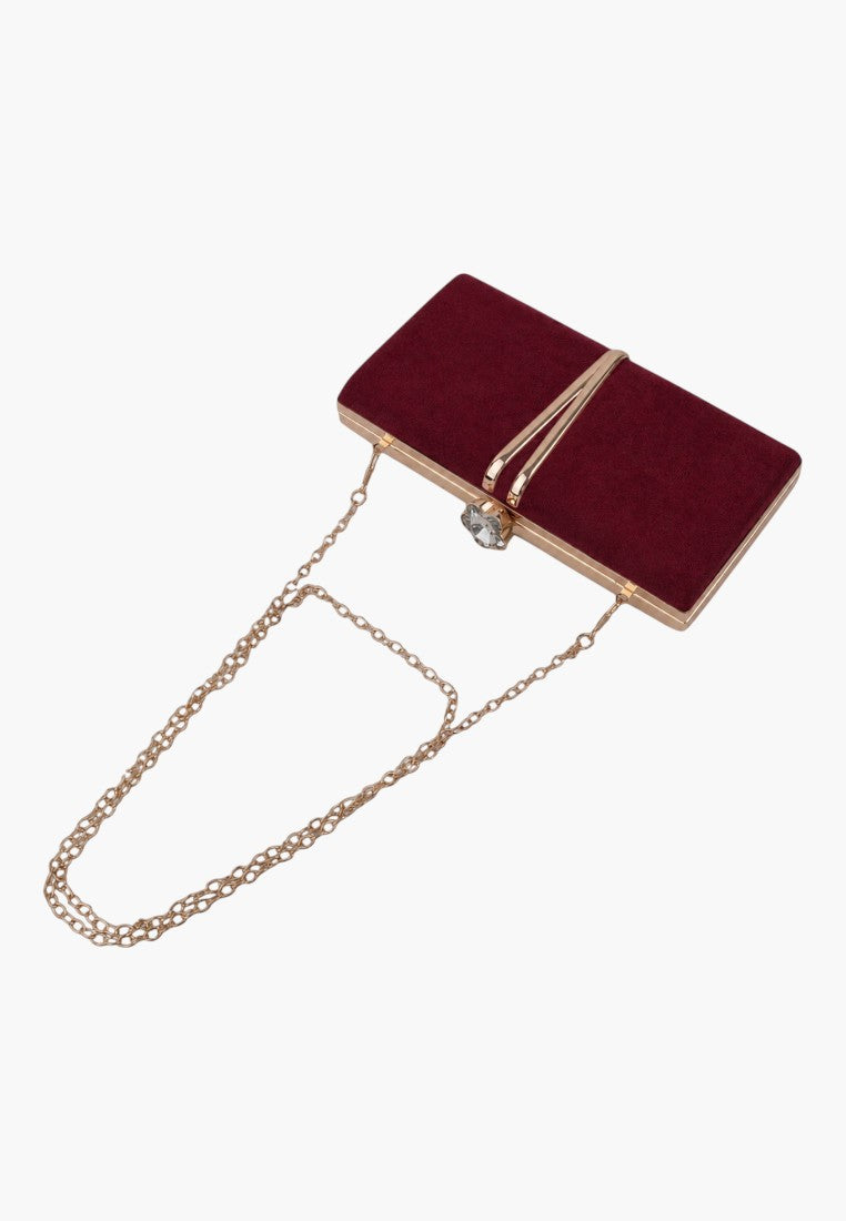 Lifestyle shot of a burgundy clutch bag with a gold chain strap on a white background