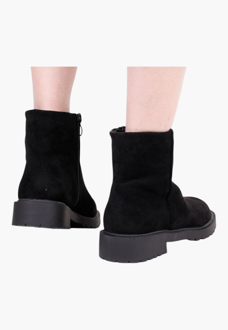 Falio black faux suede ankle boots with a flat sole and side zipper, worn on feet against a white background.