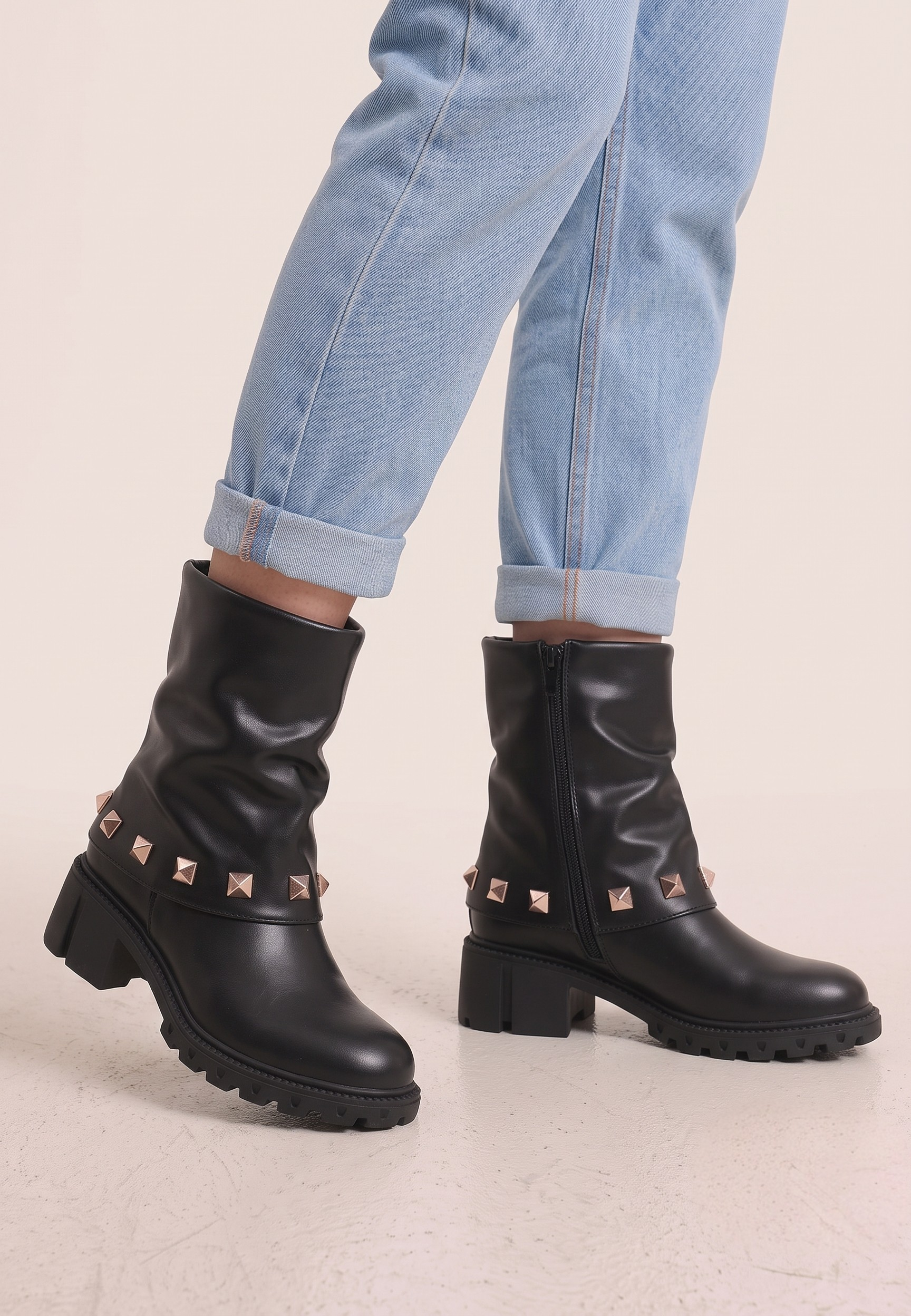 Falio black ankle boots with rose gold pyramid studs and chunky lug soles worn with cuffed blue jeans