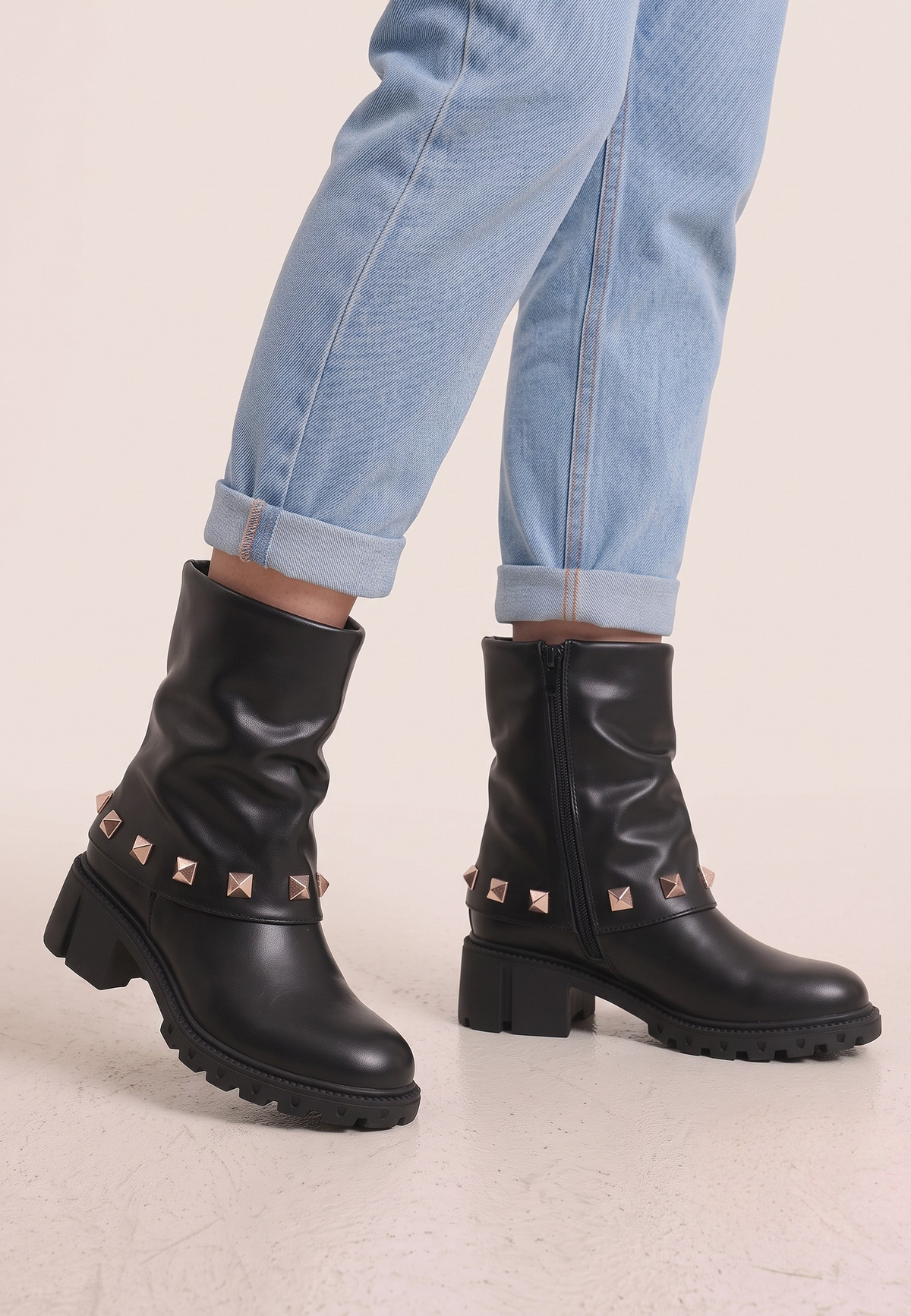 Falio black ankle boots with rose gold pyramid studs and chunky lug soles worn with cuffed blue jeans