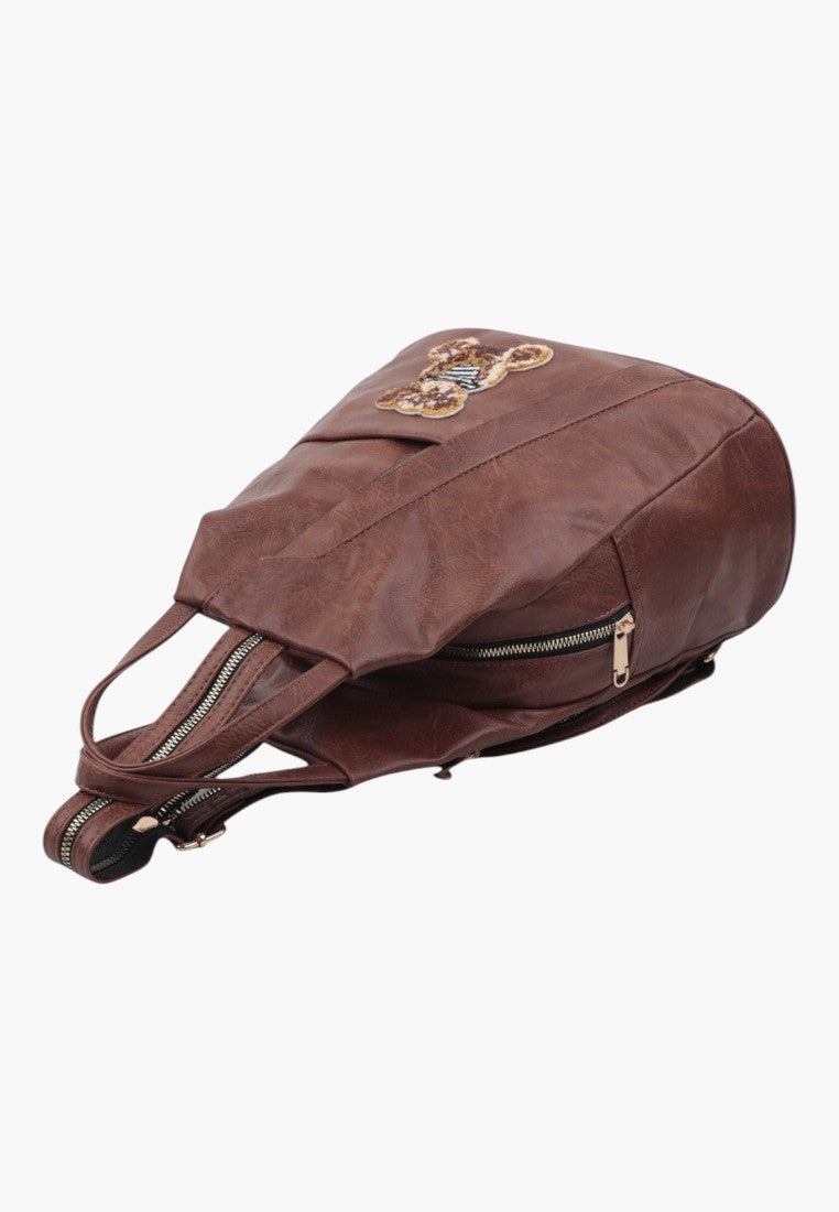 Falio brown faux leather urban backpack with a small size, multiple zipper compartments, and decorative bear patch.