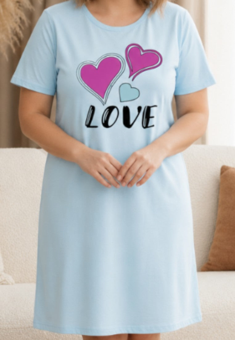Falio light blue nightgown with pink and teal heart print and LOVE text, worn by a smiling woman in a living room.