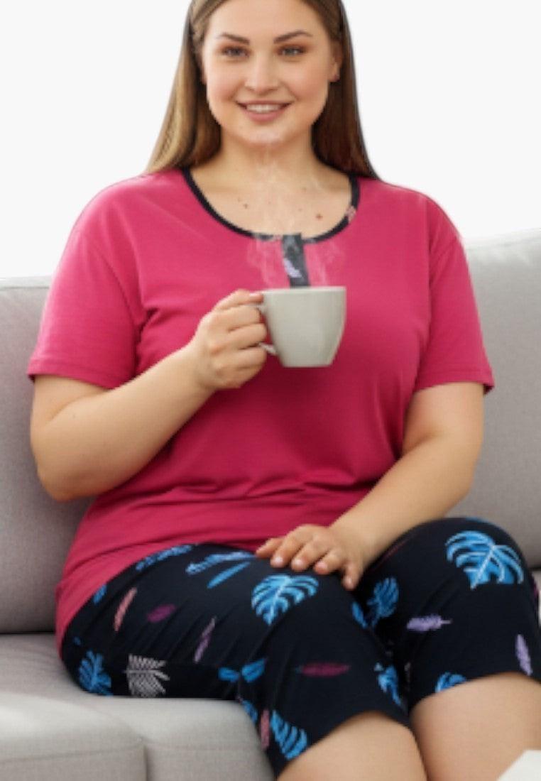 Falio plus size women's two-piece pajama set in pink with a navy trim and button detail, and black capri pants with a colorful leaf print. Made of 100% cotton.
