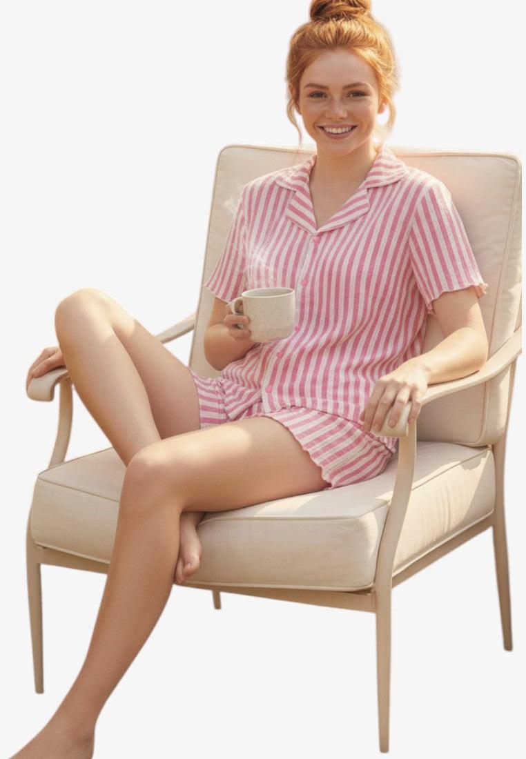 Falio pink and white striped 100% cotton pajama set with short sleeves and shorts, worn by a woman sitting in a chair.