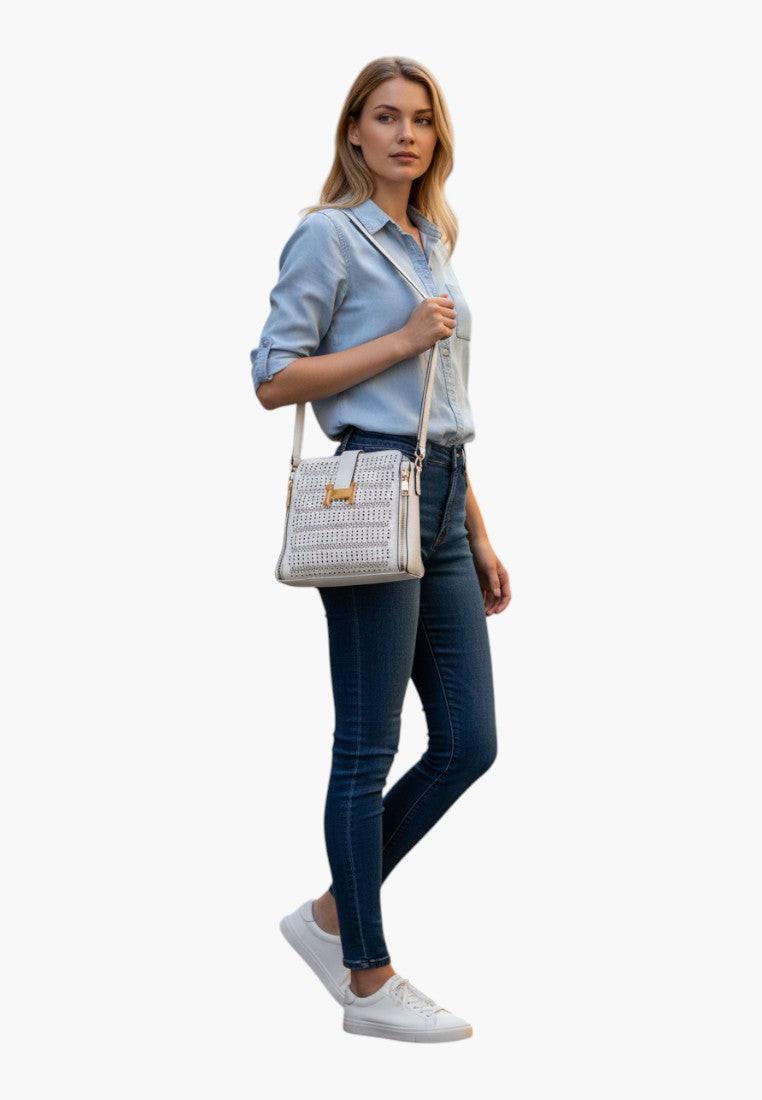 Falio white faux leather crossbody bag with perforated details and gold hardware, worn by a woman in a denim shirt and jeans.