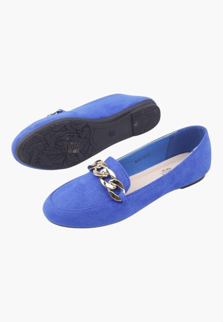 Lifestyle shot of blue suede flat shoes with decorative buckle on a white background.