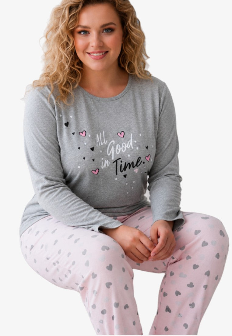 Lifestyle shot of a smiling model in a grey long-sleeve top and pink heart-patterned trousers.