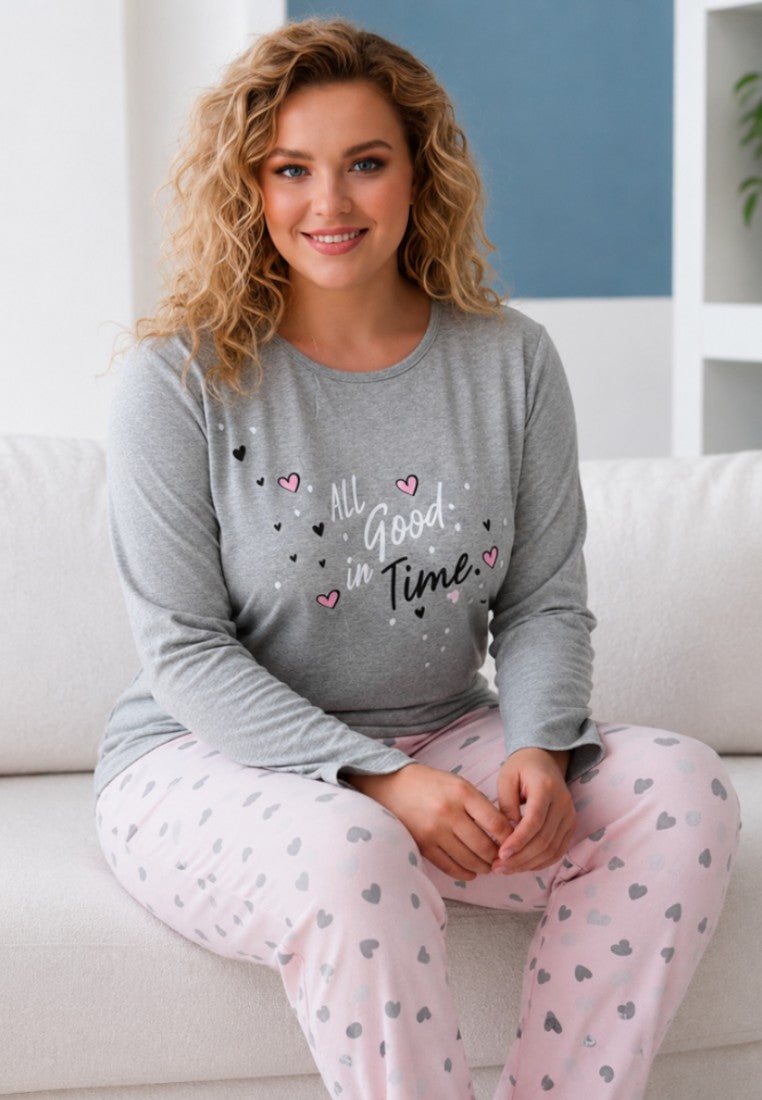 Lifestyle shot of a smiling model wearing a grey long-sleeve top and pink heart-patterned trousers.