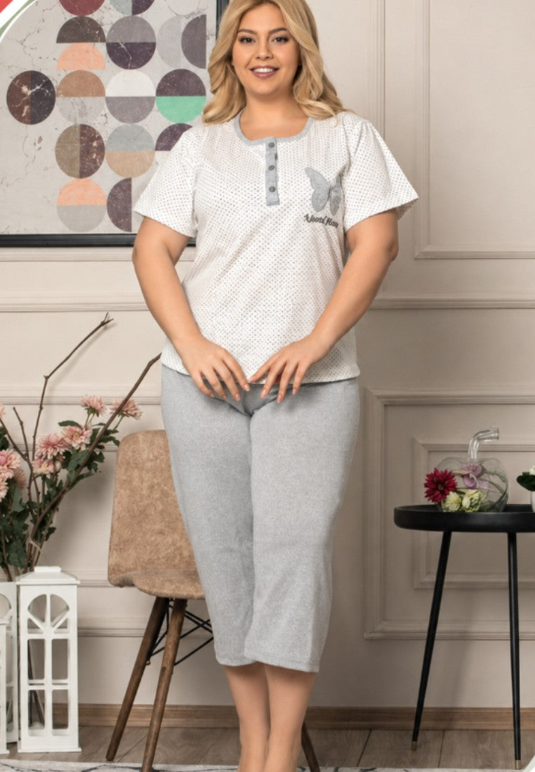 Lifestyle shot of a smiling model wearing a plus size cotton pajama set with white polka dots and grey pants.
