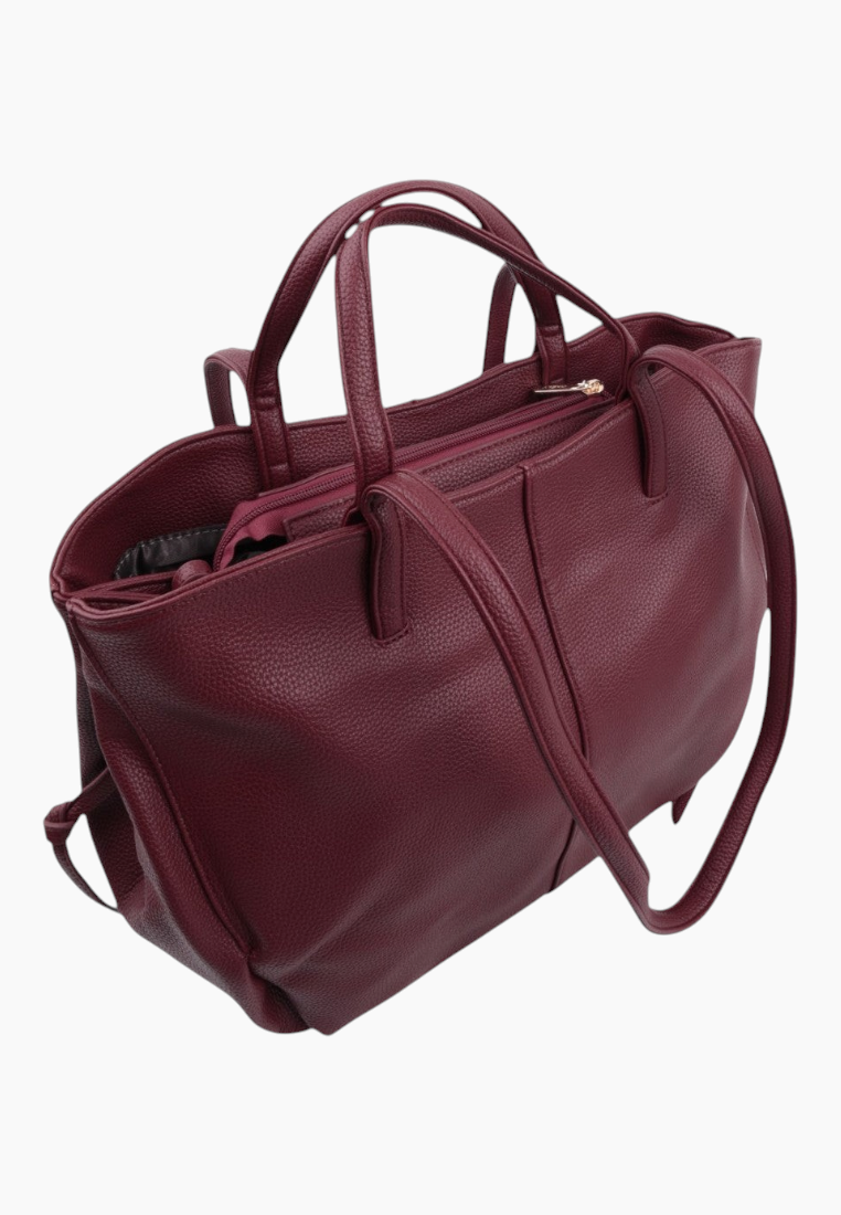 Side view of a burgundy leather handbag with double handles and a detachable strap.