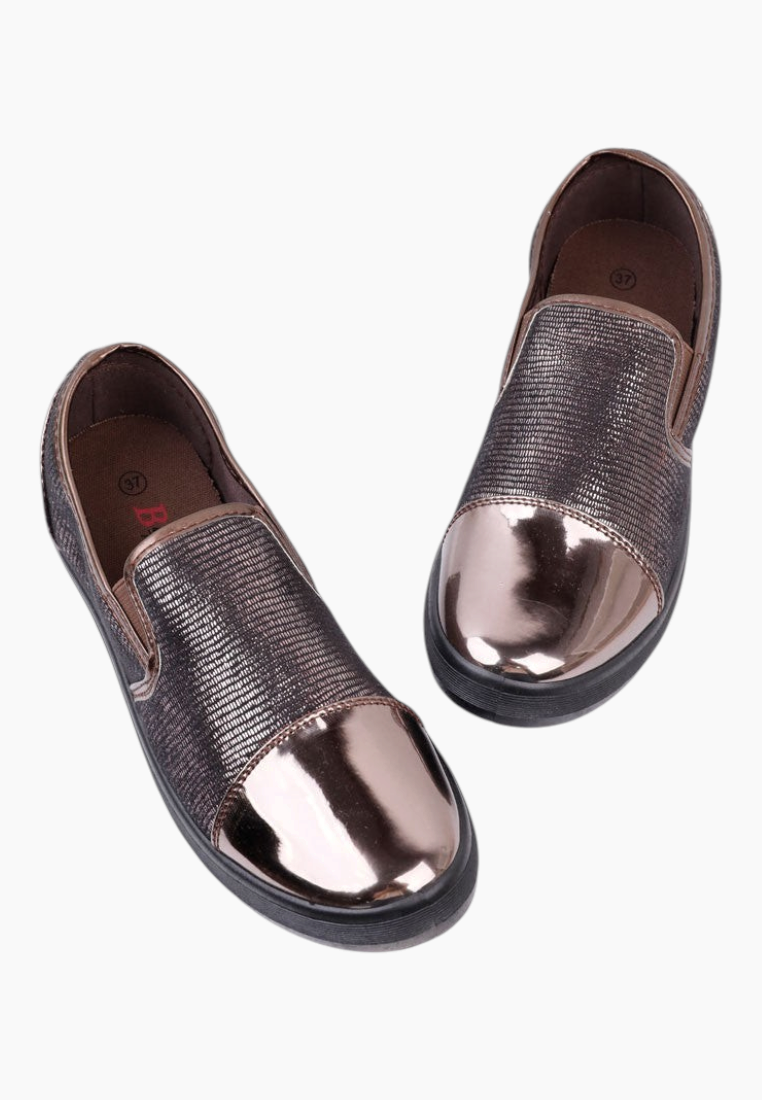 Lifestyle shot of brown slip-on shoes with metallic toe against a white background.