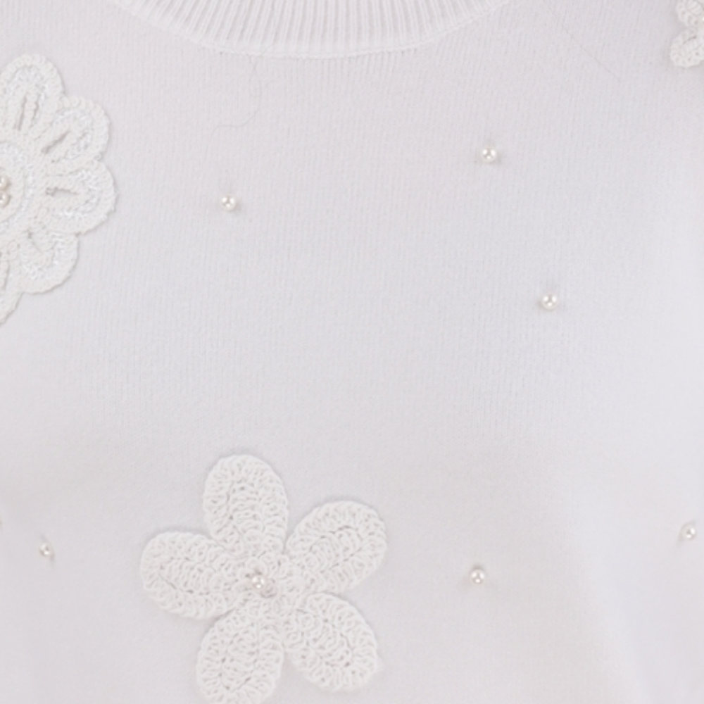 Detail view of the white sweter featuring embroidered flowers.