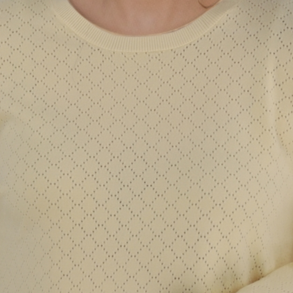 Detail close-up of the textured yellow sweter with round neckline.