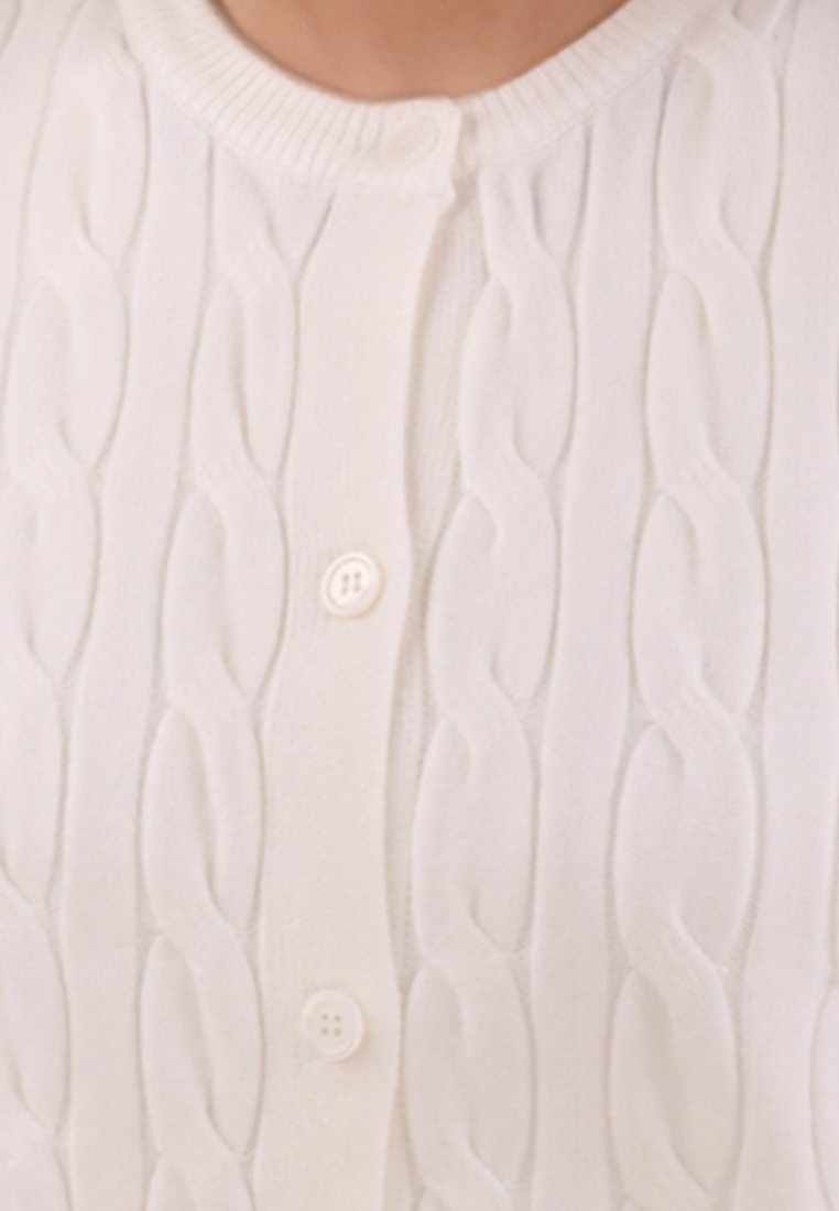 Detail view of the cream sweter showcasing the cable knit pattern.