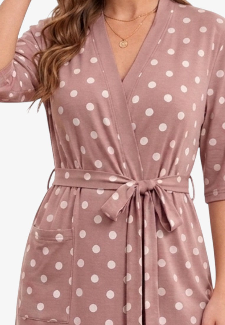 Detail view of a dusty pink cotton bathrobe with white polka dots, showing v-neck and belted waist.